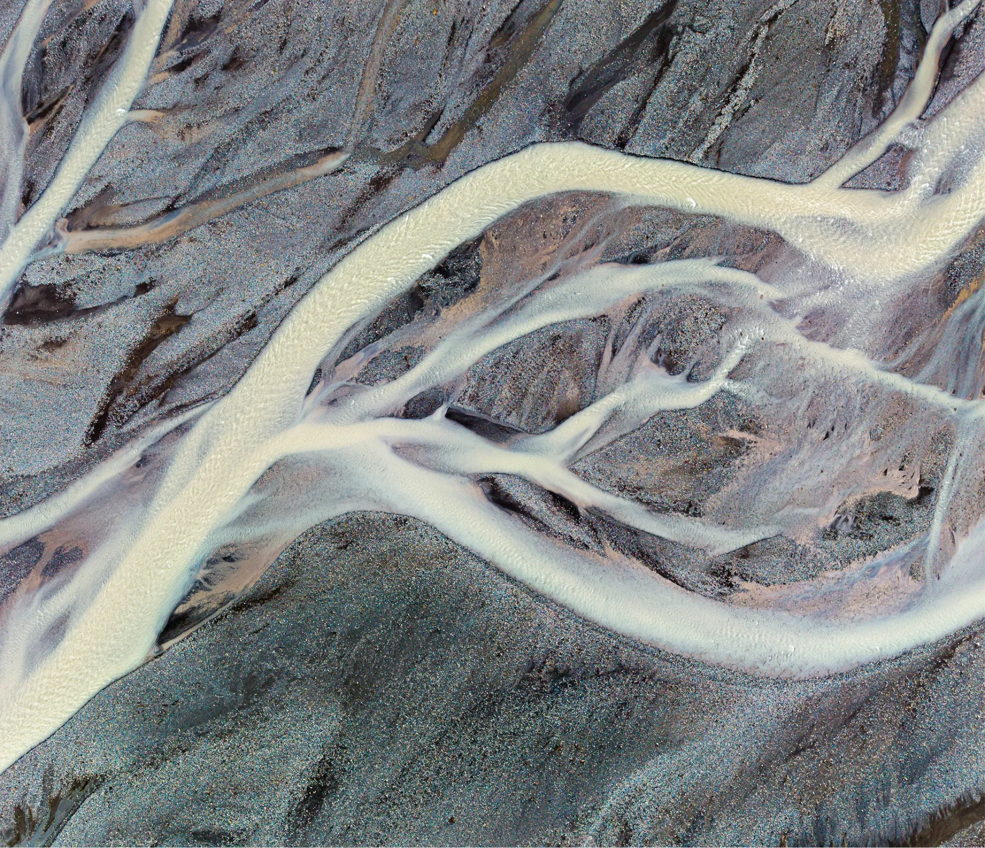 Aerial view of braided glacial river channels threading across dark volcanic sand