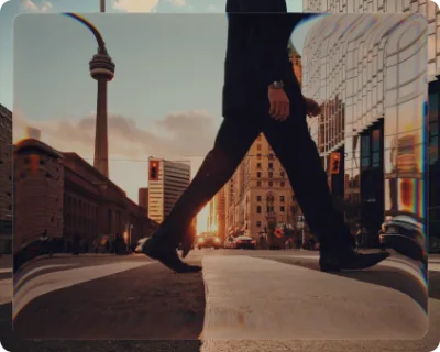 A pedestrian stepping across a downtown Toronto street at sunset, the CN Tower behind