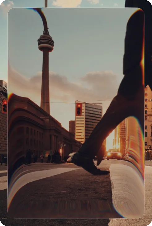 A pedestrian stepping across a downtown Toronto street at sunset, the CN Tower behind