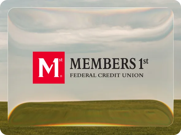 The Members 1st Federal Credit Union logo on a glass panel over a photograph of a grass field under an overcast sky